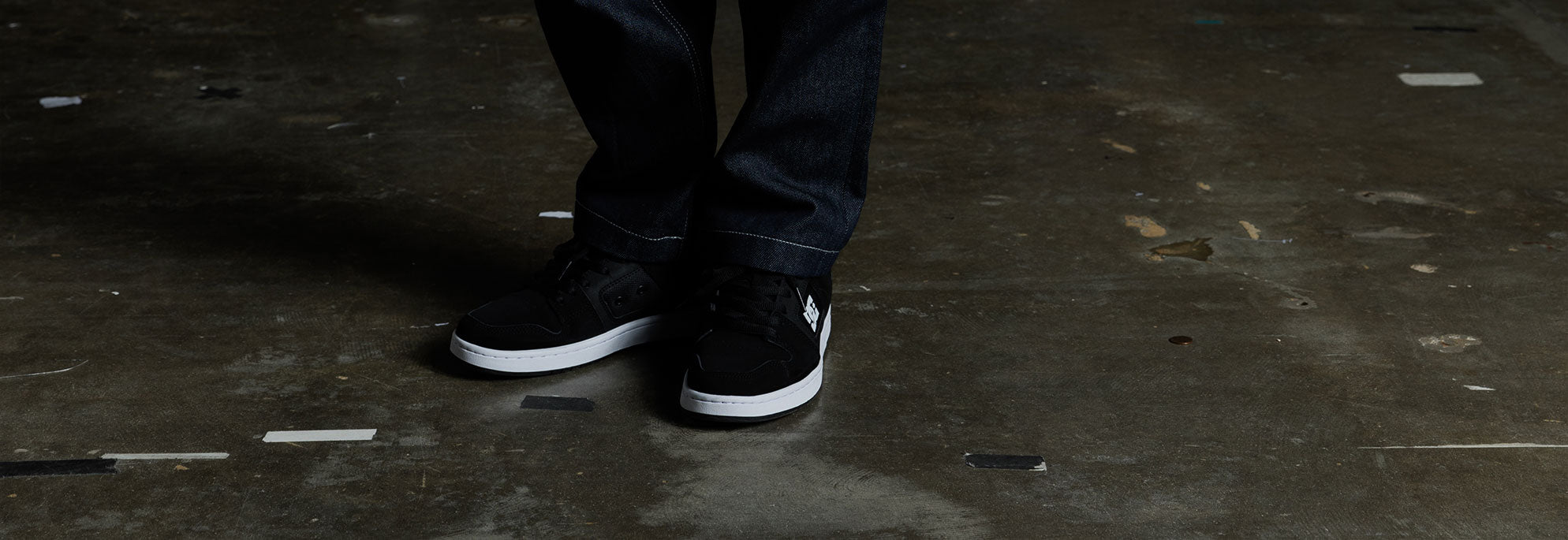 A pair of black shoes being worn by a kid on a brown floor
