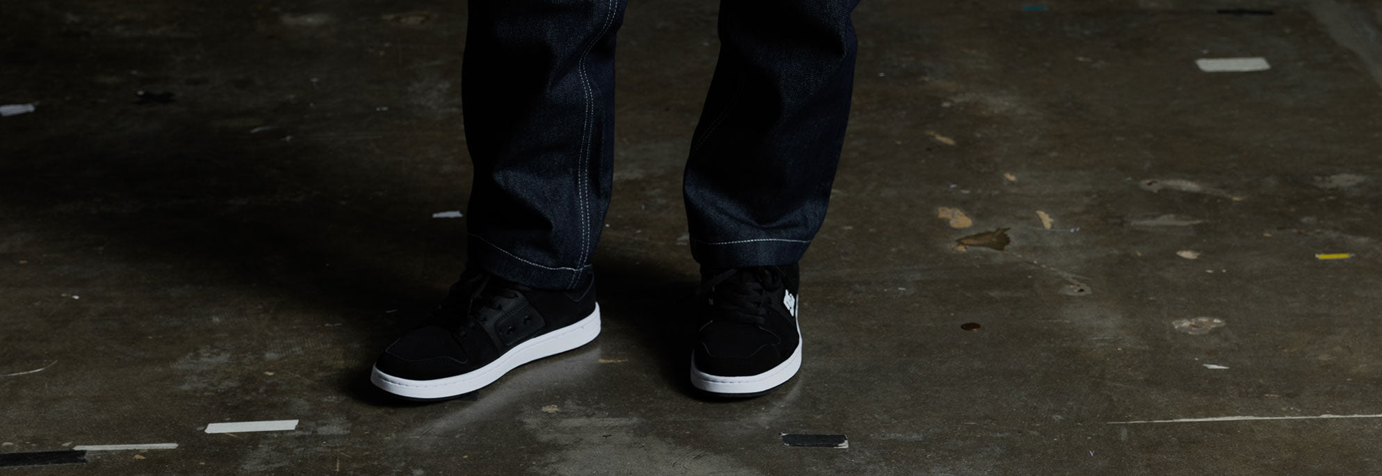 A pair of black shoes worn by a kid with jeans on