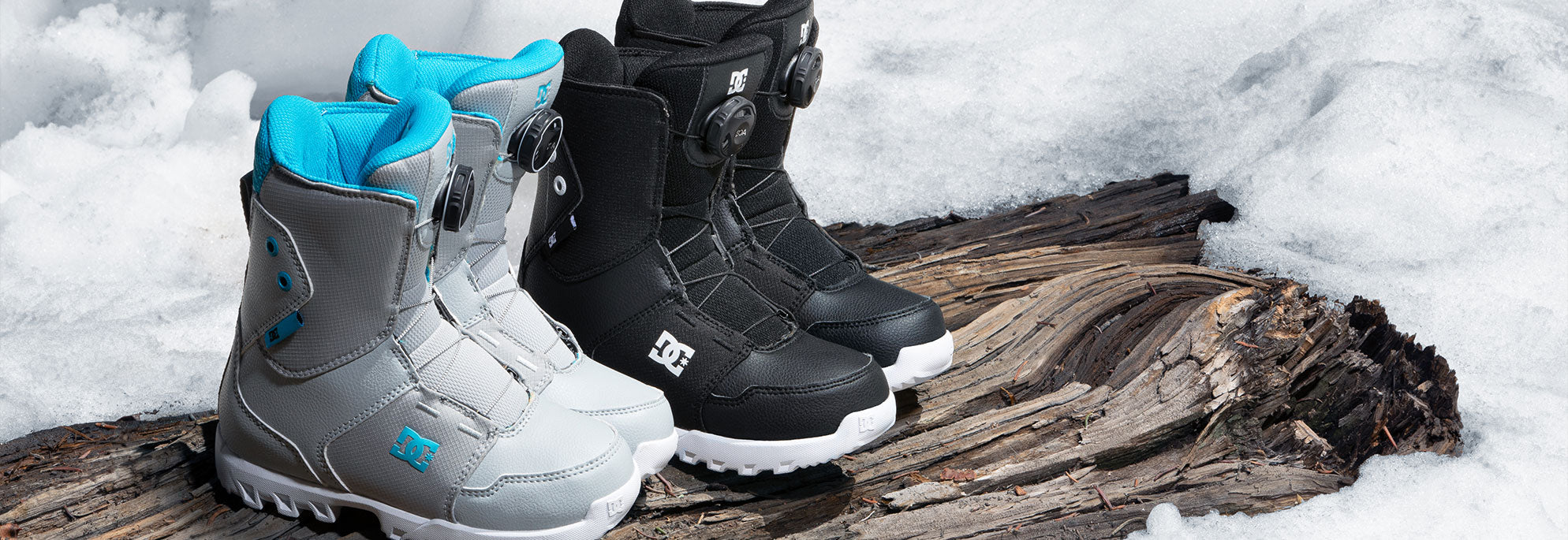 Two pairs of kids' snowboard boots on a log with a wintery background