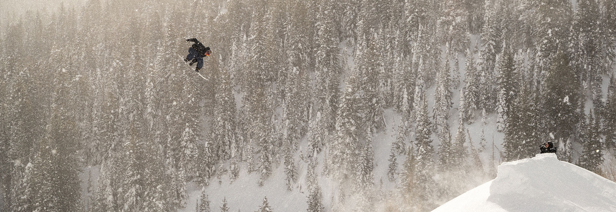 A man seen in the air doing a snowboard trick with a snowy mountain in the background