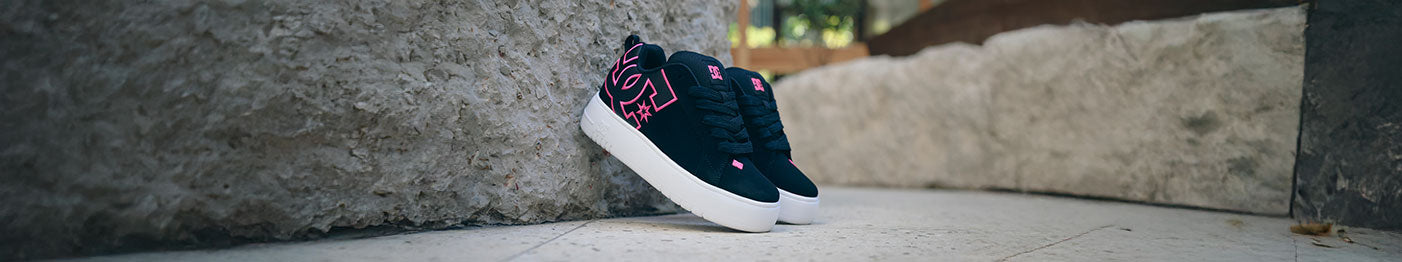 Black and white platform Court Graffik sneakers with pink logo leaning against a rocky background
