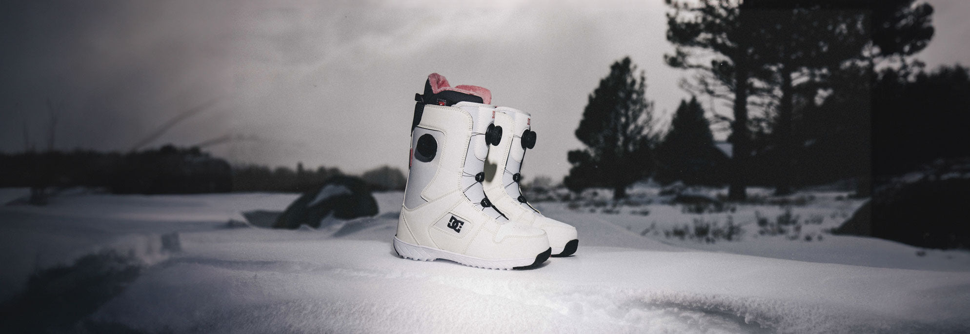 A pair of women's snowboard boots with a wintery background
