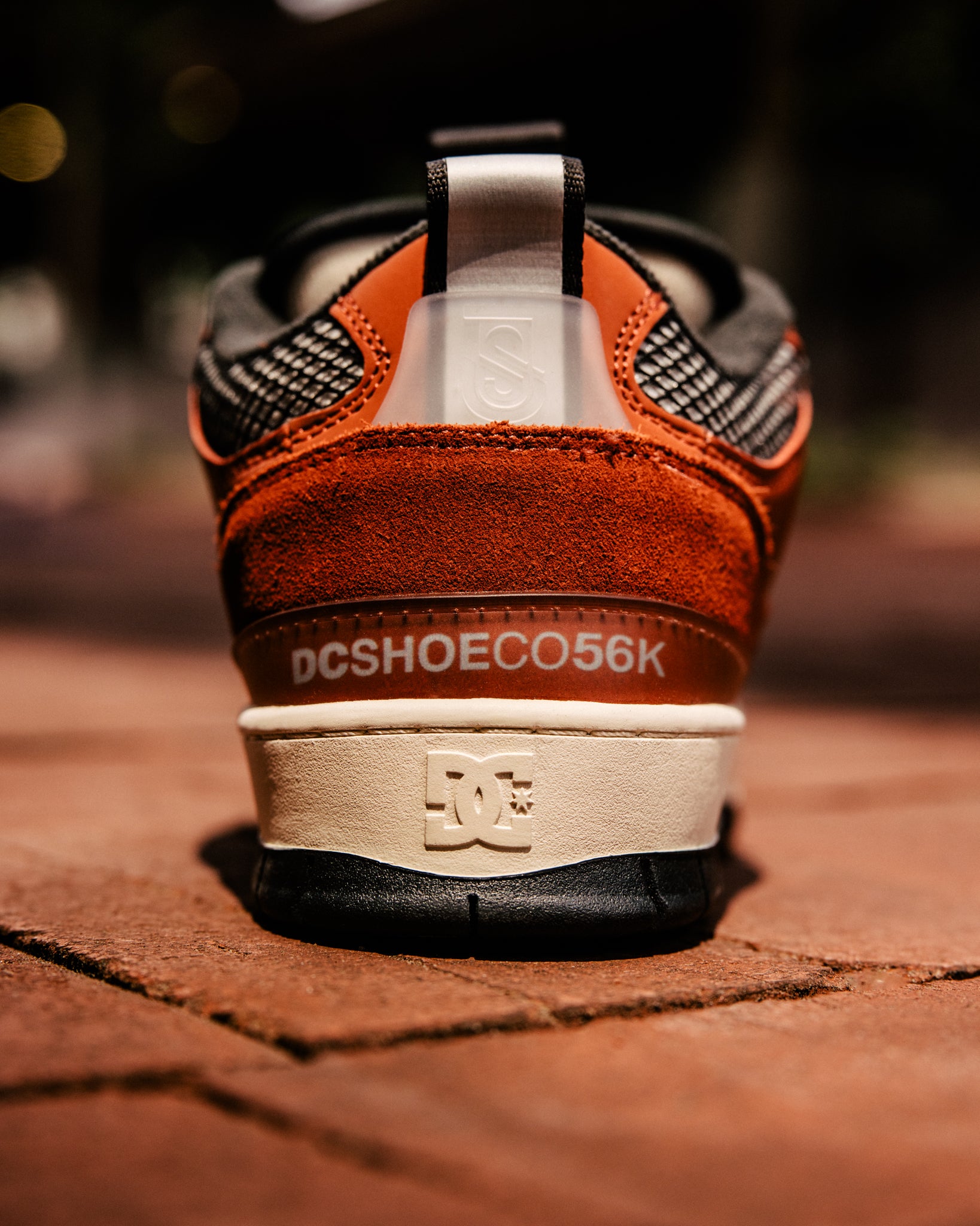 Brown and black sneaker with visible DC logo on a brick surface