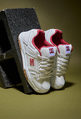 White sneakers with red accents on a dark block against a green background