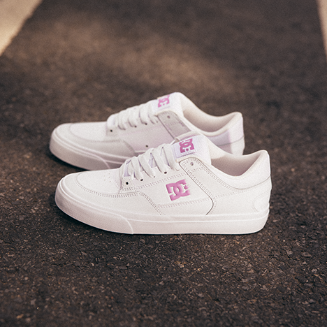 White sneakers with a pink logo on a dark textured surface