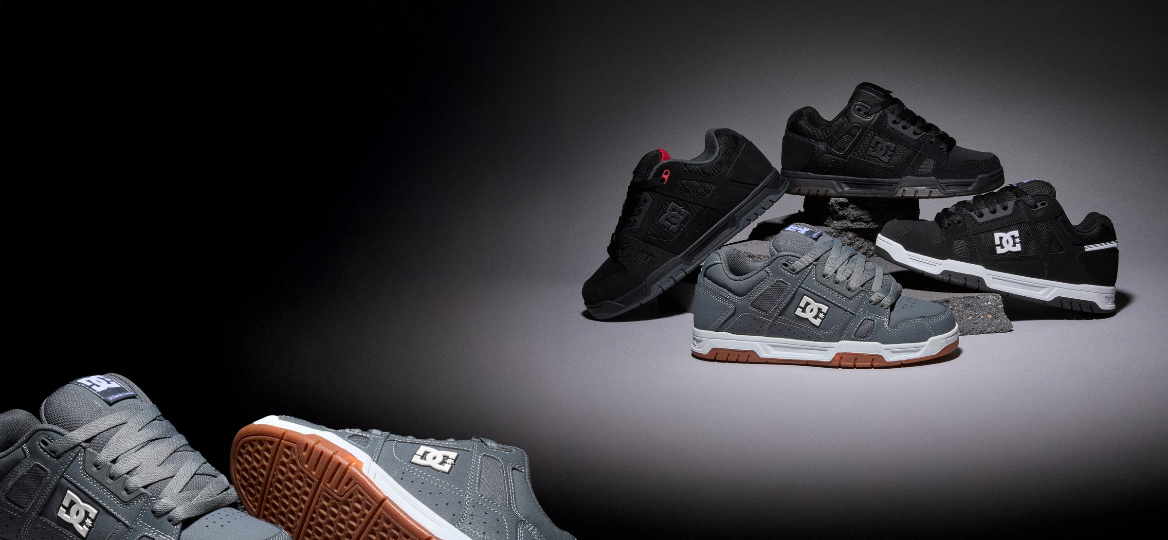 A group of DC sneakers displayed on a dark studio background, including black and gray models with white DC logos and one shoe showing a brown gum sole.