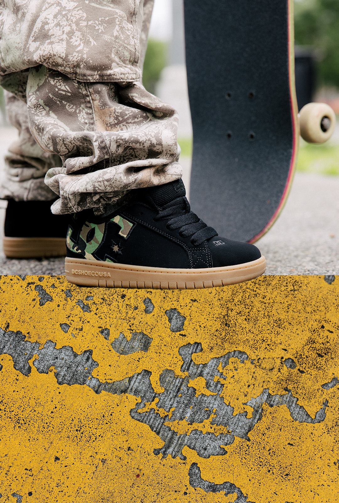 A person wearing black high-top sneakers with a green camouflage heel panel and gum soles, standing on a yellow painted curb next to a skateboard.