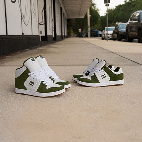 Green and white sneakers on a concrete surface with a building and cars in the background