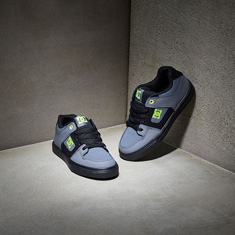 Pair of gray and black sneakers with green accents on a concrete floor.