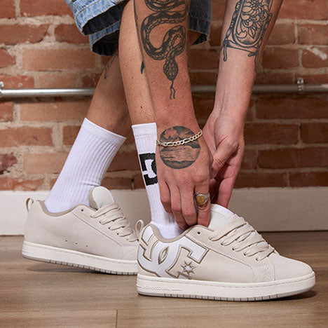 Person adjusting white sneakers with a brick wall background