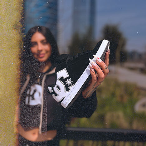 Woman holding a black and white shoe with a DC logo, outdoors.