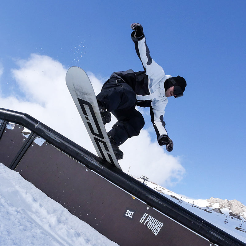 Person snowboarding off a rail with mountains and blue sky in the background