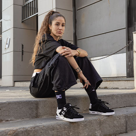 Person sitting outside on stairs in a black outfit and black and white sneakers
