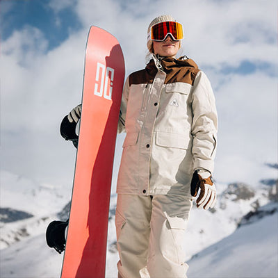 Person in winter gear holding a red snowboard with a mountainous background
