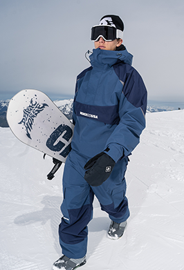 A person standing on a snowy mountain wearing a navy and blue snowsuit with black gloves, white goggles, and a black beanie, while holding a white snowboard with a black graphic. The brand name 'HONHOUASA' is visible on the chest of the snowsuit.