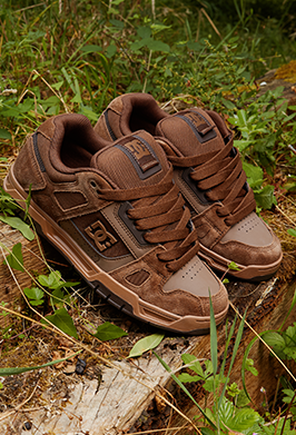 A pair of brown suede and mesh low-top sneakers resting on a weathered log outdoors in a grassy, wooded setting.