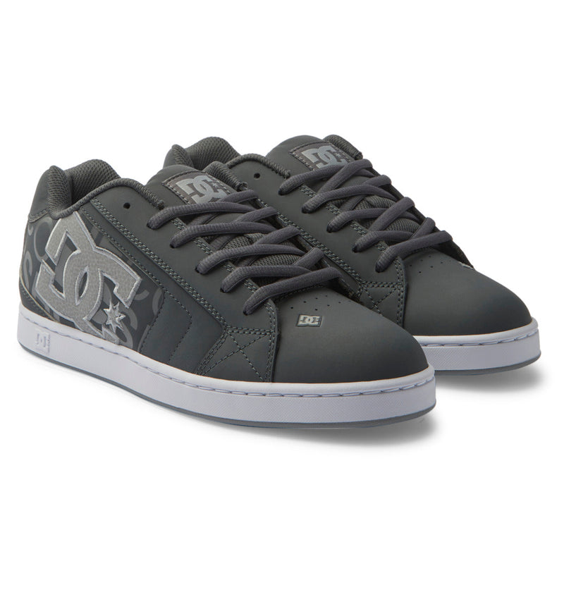 The DC Shoes Men's Net Shoes feature a dark gray design with black laces, white soles, and a prominent white DC logo on the side, providing all-day comfort. Shown on a plain white background.