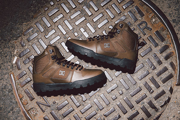 Brown boots with black soles on a metal manhole cover