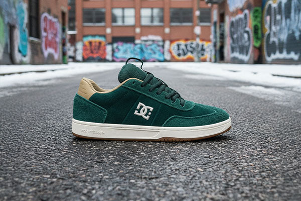 Green sneaker with a white sole on an urban street with graffiti.