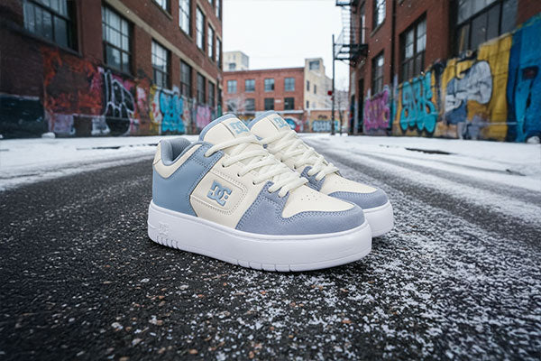 Blue and white platform sneakers on a snowy street with graffiti-covered buildings in the background