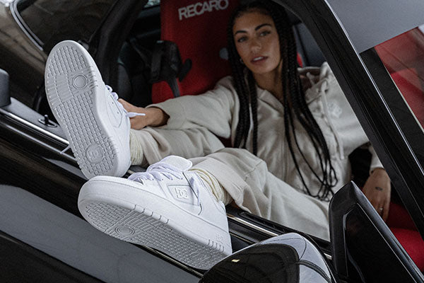 Woman sitting in a car with feet out of the window wearing white sneakers.