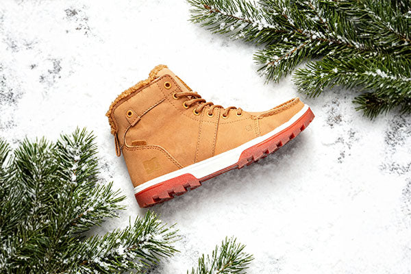 Tan winter boot on a snowy background with pine branches