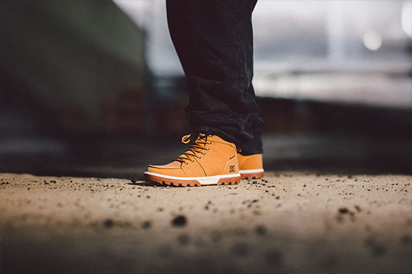 Orange boots worn with dark pants on a blurred outdoor background