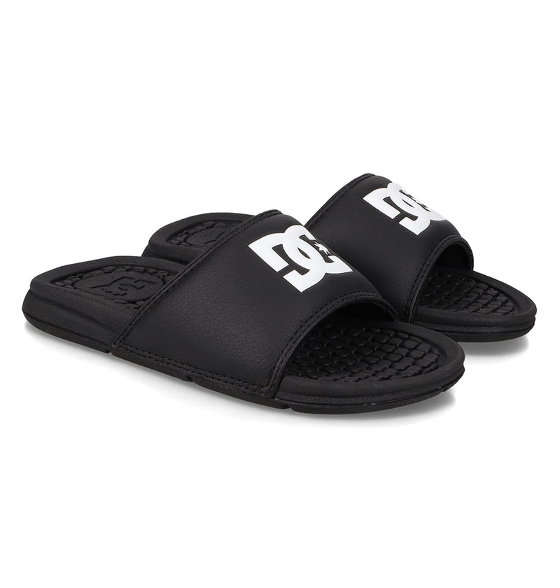A pair of Kids' Bolsa Slides from DC Shoes in black with open toes and bold white DC logos on the straps, shown on a white background.
