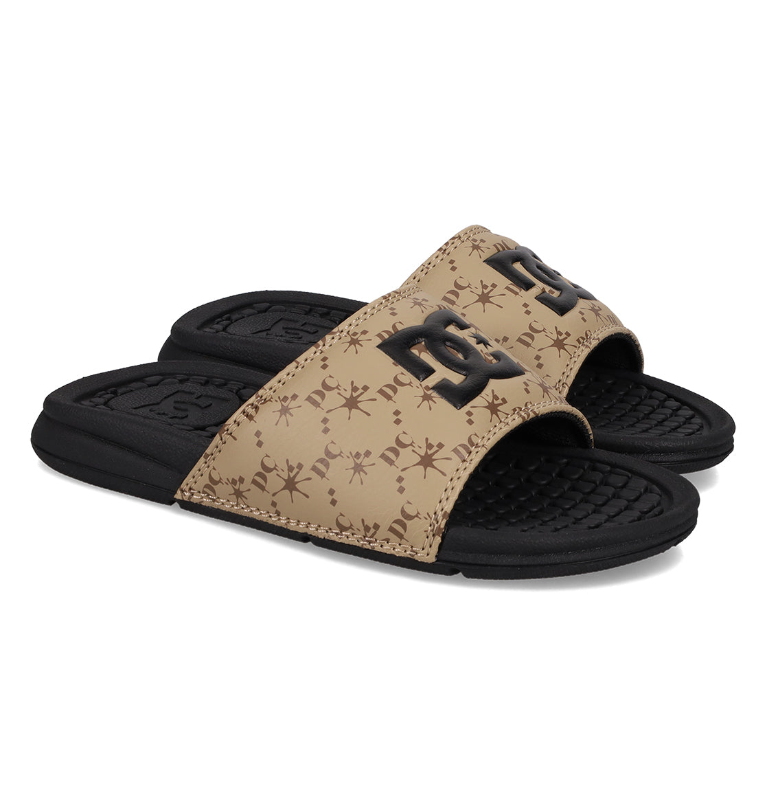 A pair of Kids' Bolsa Slides by DC Shoes in black and tan, featuring textured soles, a brown strap with a repeating logo pattern, and a large black DC Shoes logo on top.