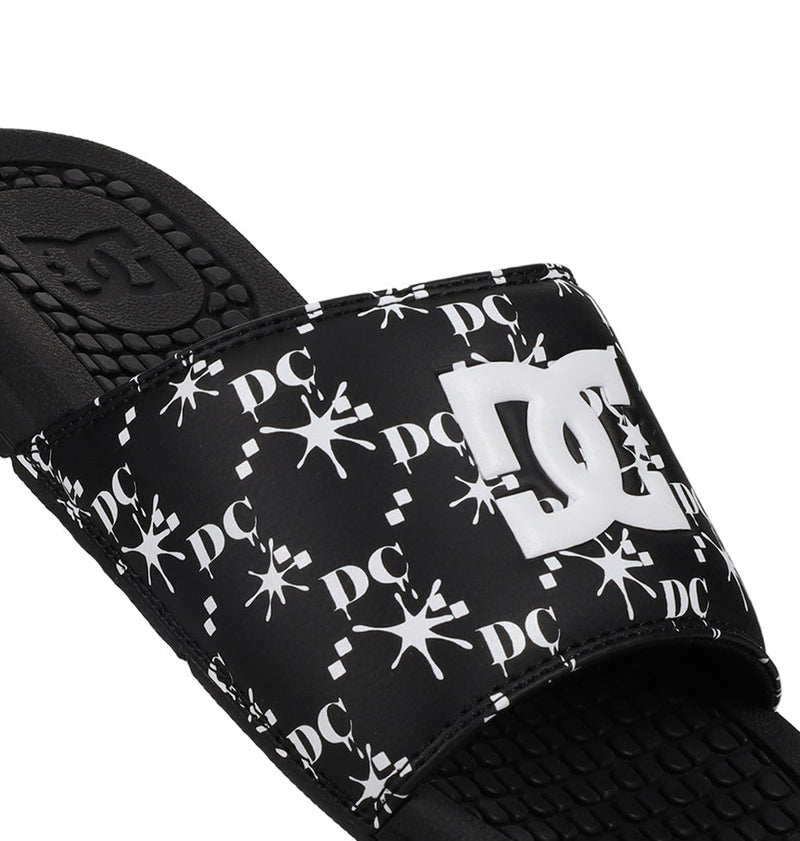A close-up of the Men's Bolsa Slides by DC Shoes shows a white logo and star pattern on the strap, plus a textured footbed—ideal for relaxing after skating. Part of the durable rubber sole is also visible.