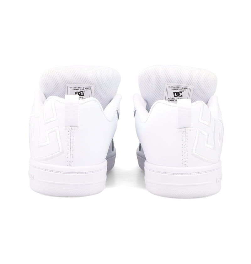 The Kids' Court Graffik Shoes by DC Shoes are white sneakers shown from the back, featuring embossed heel patterns, visible inner tongue labels, white soles, and stitching accents for a classic skate-inspired look.
