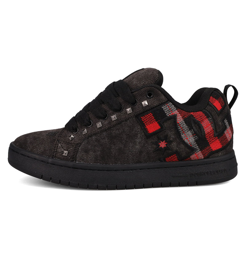 The DC Shoes Men's Court Graffik SE features a black textured fabric upper with premium materials, black laces, silver studs, and red and gray plaid accents on the side and heel. It has a black sole and a subtle star detail in the design.