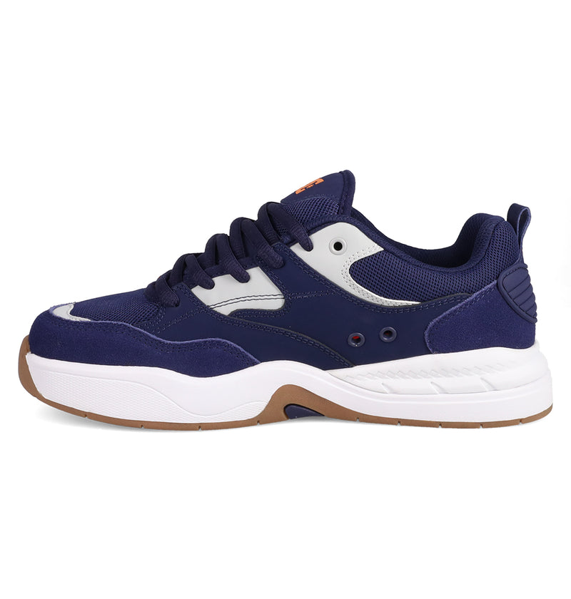 The Men’s DC Ascend S Shoes by DC Shoes feature a chunky navy blue and white design with mesh and suede panels, thick white sole, navy laces, and brown rubber outsole accents, inspired by Josh Kalis and classic DC DNA.