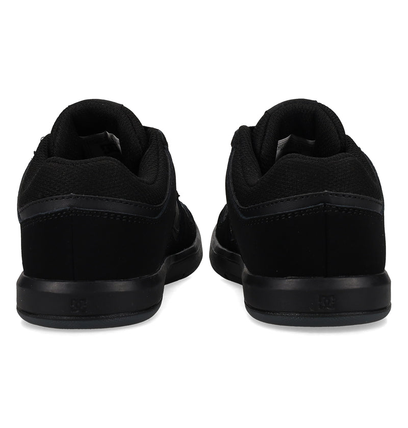 A pair of Kids' DC Shoes Cure Elastic Shoes by DC Shoes in black, shown from the back to highlight the heels and soles, featuring a simple and sleek low-top design.