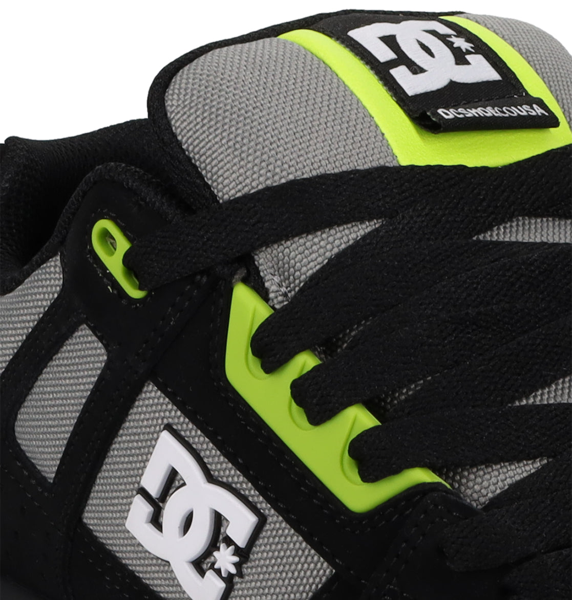 Close-up of DC Shoes Men's Stag Shoes featuring a gray mesh dynamic upper, black accents, neon yellow eyelets, and white DC Shoes logos on the side and tongue. Durable cupsole ensures lasting support.