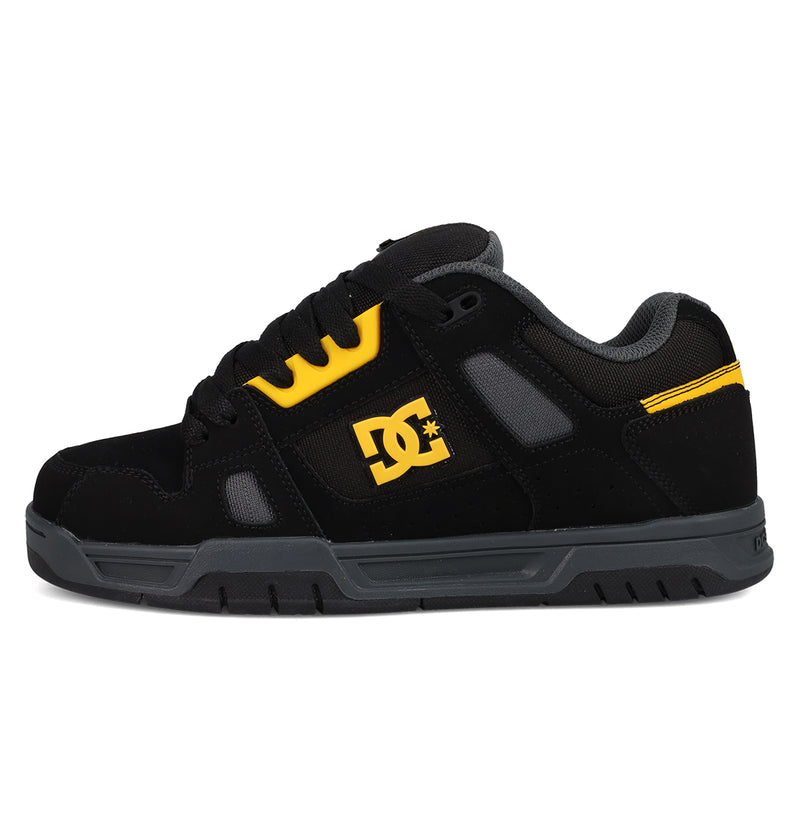 The Men's Stag Shoes by DC Shoes are black and gray skate sneakers with yellow accents, featuring the DC logo, black laces, gray rubber cupsole, a padded collar for comfort, and a low-top design inspired by skate culture.