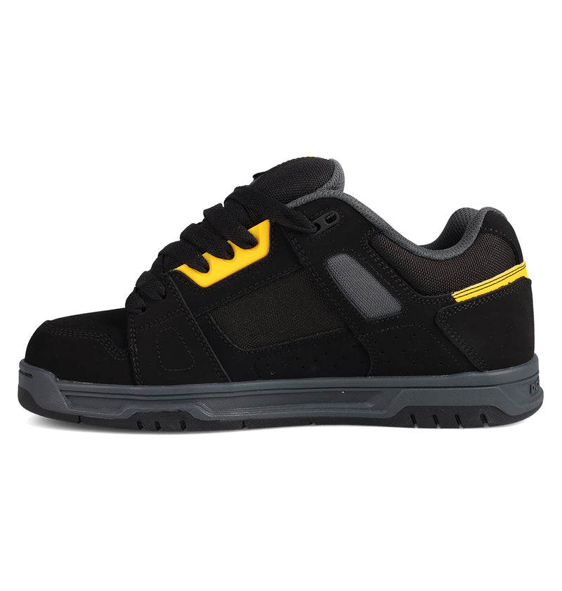 The DC Shoes Men's Stag Shoes are black athletic sneakers with gray and yellow accents, a thick cupsole, padded tongue, and mesh panels, inspired by skate culture and DC Stag. Shown in side profile on a white background.