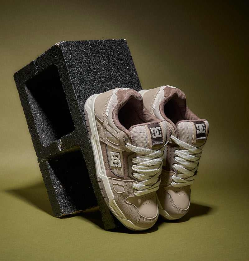 Pair of beige sneakers with white soles on a green background