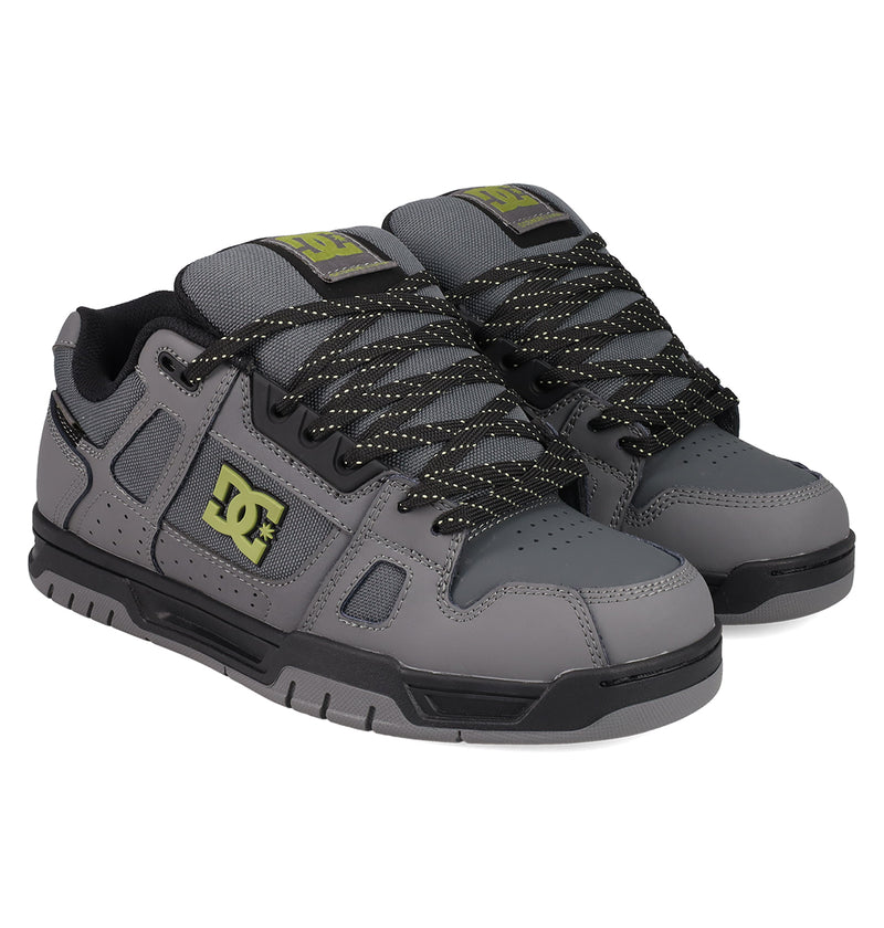 The DC Shoes Men's Stag Shoes feature a gray design with black detailing, black-and-white speckled laces, a durable cupsole, and yellow DC branding on the side, tongue, and heel tab—highlighting authentic skate style.