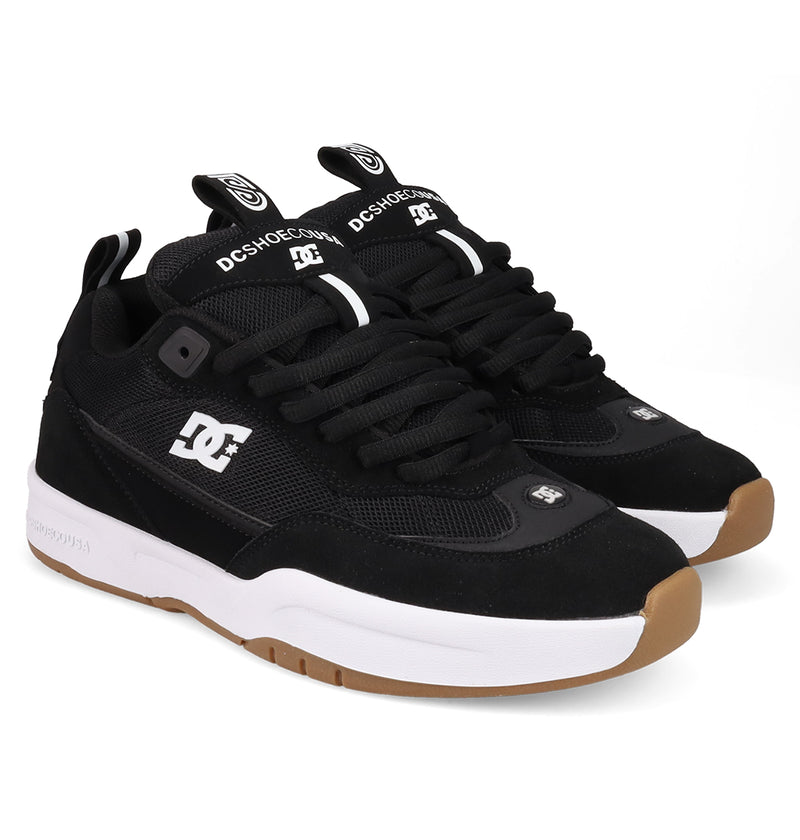 The Men's JS-2 Shanahan Pro Skate Shoes by DC Shoes feature black uppers, white soles, gum outsoles, black laces, and white DC branding, inspired by DC heritage and the JS 2 line. They're shown angled on a white background.