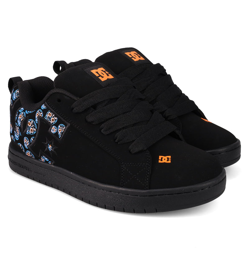 A pair of Men’s Court Graffik Day Of The Dead sneakers by DC Shoes—featuring wide black laces, striking orange DC logos, and colorful skull patterns on the sides near the heel, designed as part of the vibrant Día de los Muertos Collection.