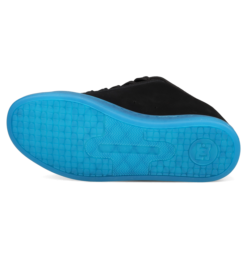A black Women’s Court Graffik Beveled Shoe by DC Shoes is shown from the side, highlighting the bright blue textured sole with a patterned design and a raised B logo near the heel. This sneaker features signature DC branding and a puffy silhouette for added style and comfort.