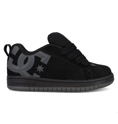 A side profile view of the DC Shoes Kids’ Court Graffik Beveled Special Edition features a black skate shoe with a puffy silhouette, thick laces, a large gray DC logo on the side, and a dark gray sole, displayed on a white background.