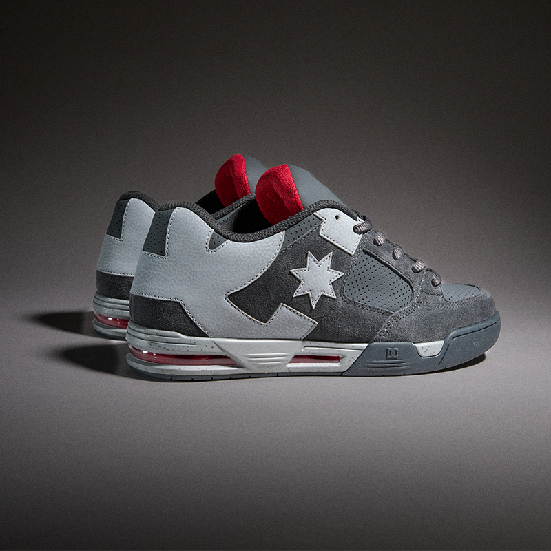 A pair of low-top sneakers in gray suede and mesh with a white star logo on the side, red tongue inserts, and a translucent red air unit on the sole, photographed on a dark gray gradient studio background.