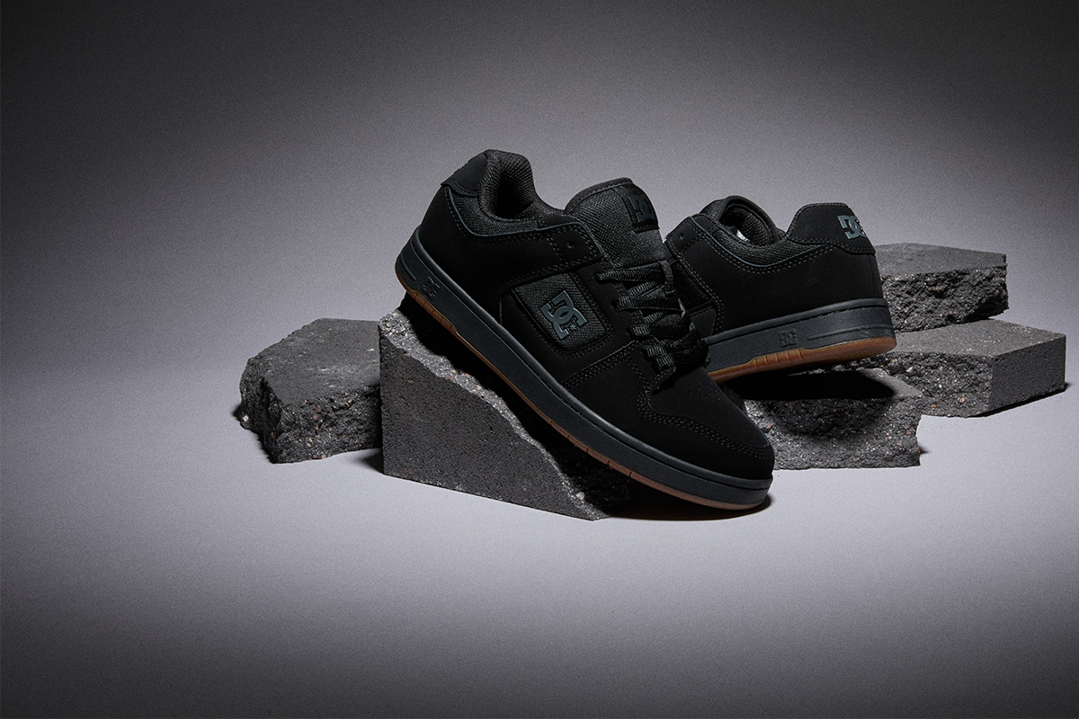 Pair of black DC skate shoes with gum soles displayed on textured concrete blocks in a studio setting.