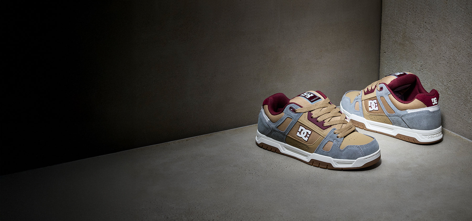 Pair of red, brown and gray sneakers on a gray surface with a dark background