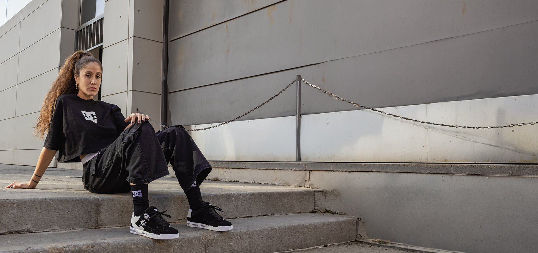 Person sitting on steps wearing black outfit with visible brand logo.