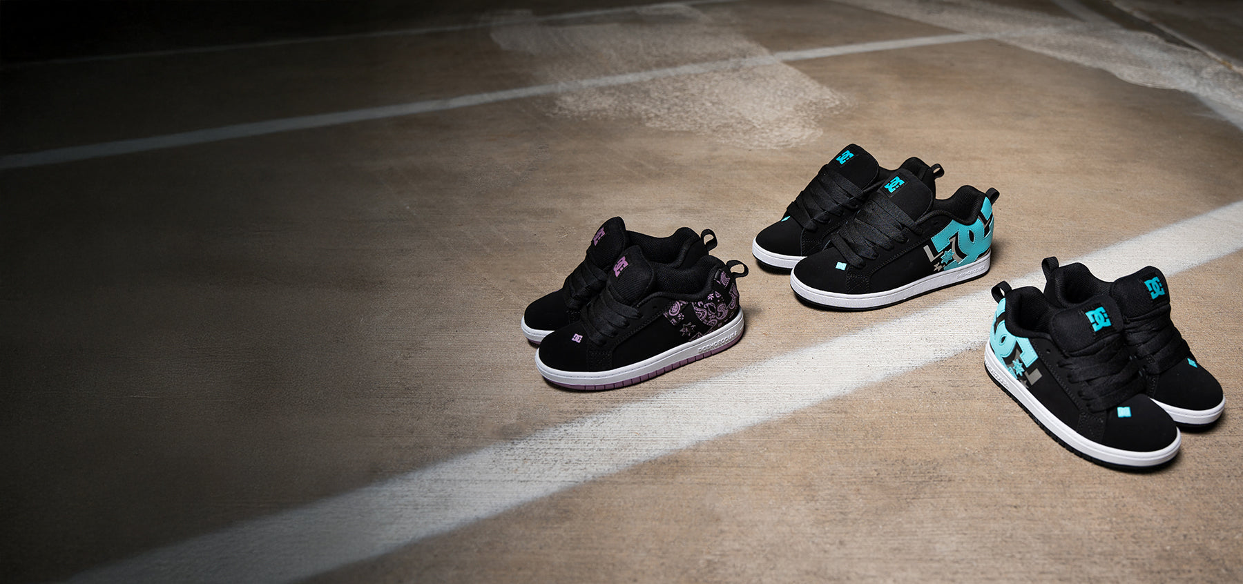 Three pairs of black sneakers with teal and pink accents on a concrete floor.