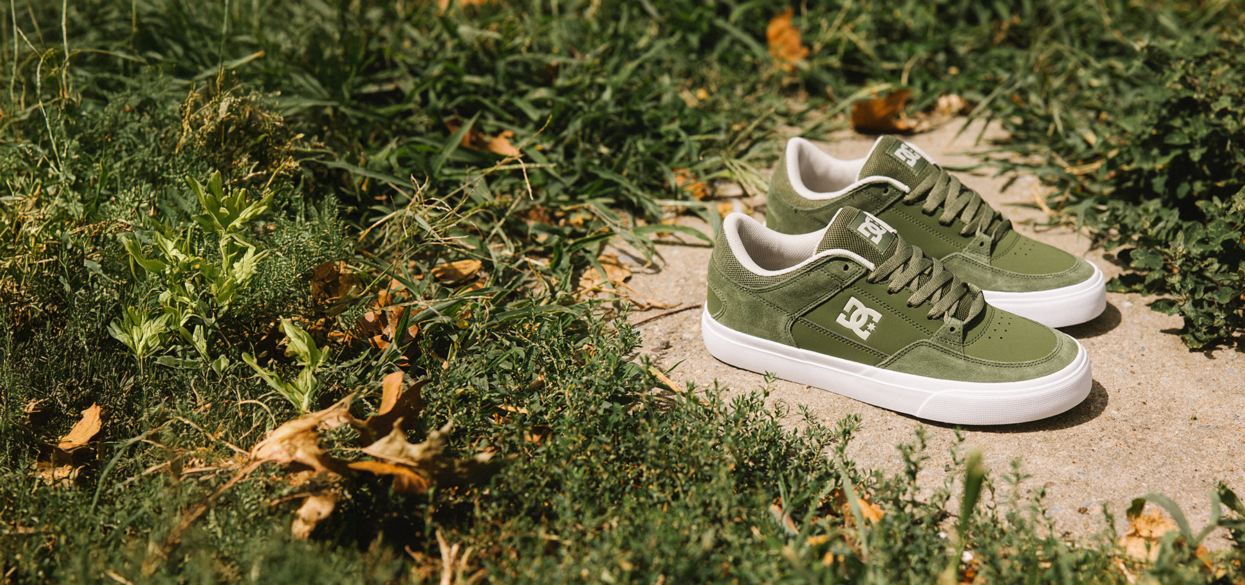 Green sneakers with white soles on a stone surface surrounded by grass and leaves.
