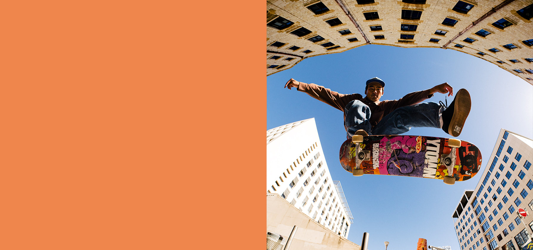 Skateboarder performing a trick in an urban setting with buildings in the background next to orange colorblock